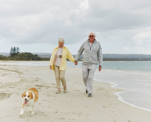 An older couple walking their dog along the beach in Dunsborough, Western Australia