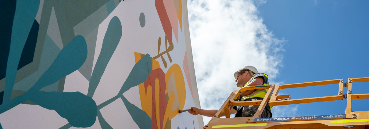 Man on a cherry picker painting a colourful mural on a wall