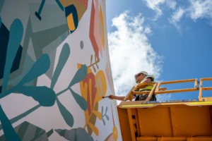 Man on a cherry picker painting a colourful mural on a wall