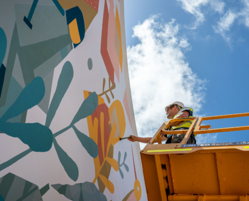 Man on a cherry picker painting a colourful mural on a wall