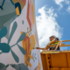 Man on a cherry picker painting a colourful mural on a wall