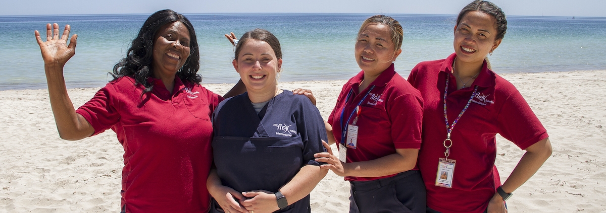 4 women in aged care uniforms posing happily on the beach in Busselton