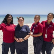 4 women in aged care uniforms posing happily on the beach in Busselton