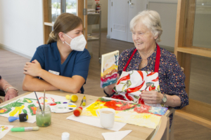 Carer with an aged care resident looking at an art class painting