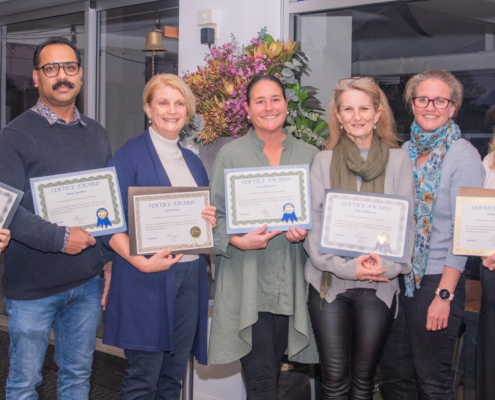7 people standing in a line smiling and holding award certificates