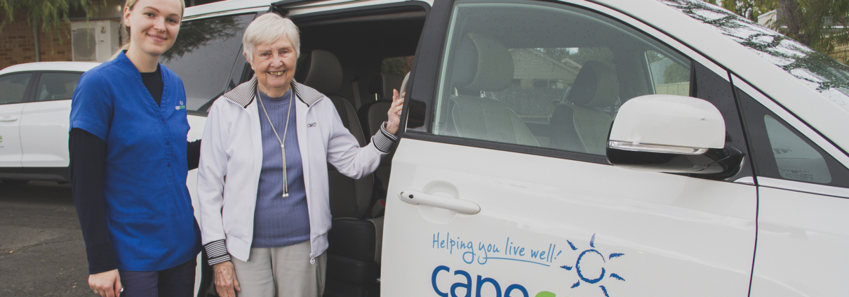 Young woman helping an older woman into a minibus marked Capecare