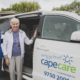Young woman helping an older woman into a minibus marked Capecare