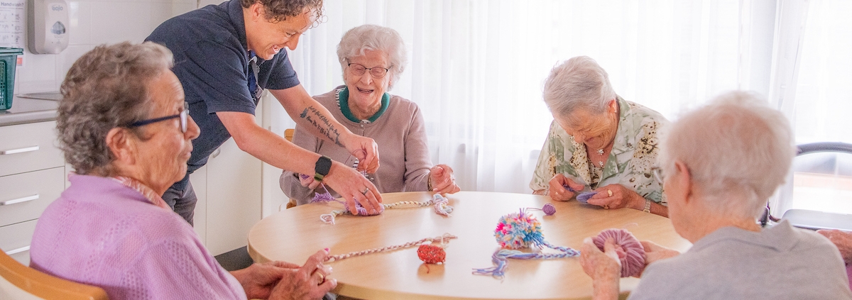 4 older ladies sitting at a table making pom poms with an aged care facility helper