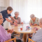 4 older ladies sitting at a table making pom poms with an aged care facility helper