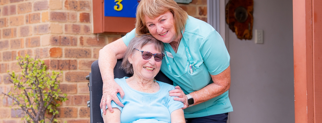 Lady in a wheelchair being hugged by a friendly nurse