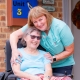 Lady in a wheelchair being hugged by a friendly nurse