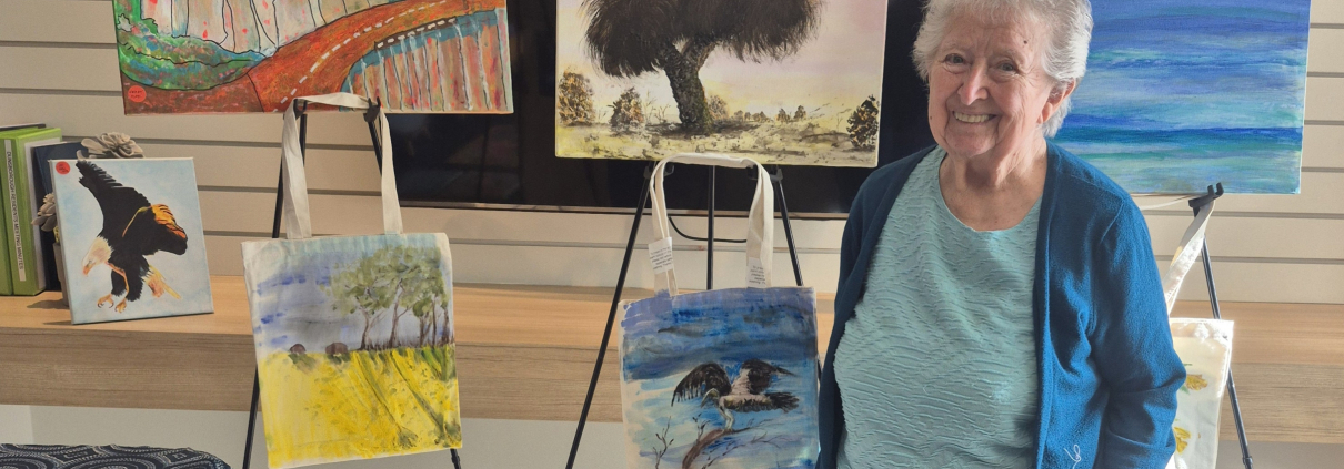 Smiling older lady in front of a display of paintings on easles and on the wall
