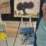Smiling older lady in front of a display of paintings on easles and on the wall