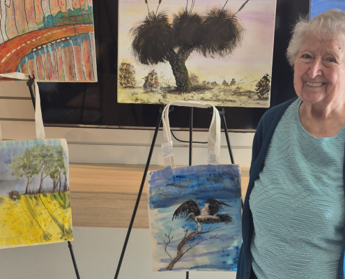 Smiling older lady in front of a display of paintings on easles and on the wall