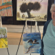 Smiling older lady in front of a display of paintings on easles and on the wall
