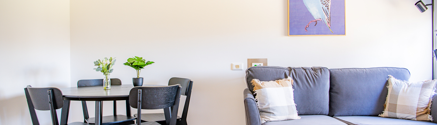 Bright room with small round dining table and comfortable sofa with bright budgie painting on the wall.