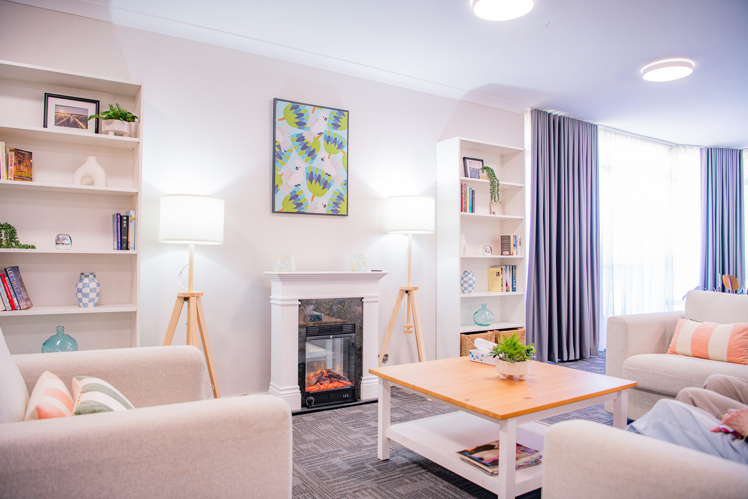 Bright airy living room with 3 sofas facing a fireplace with lit fire and bookcases