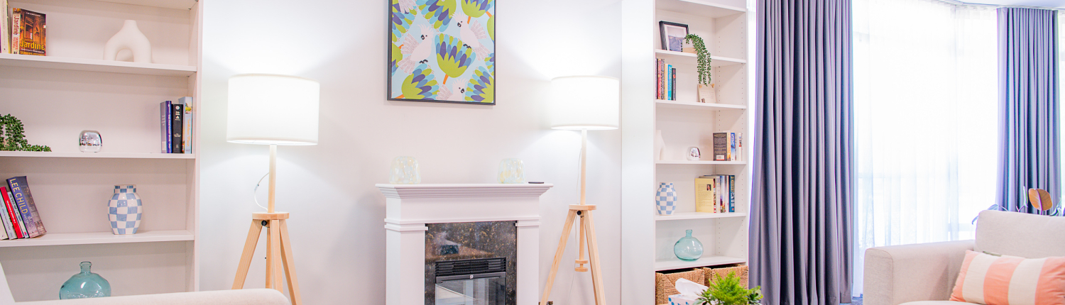 Bright airy living room with 3 sofas facing a fireplace with lit fire and bookcases