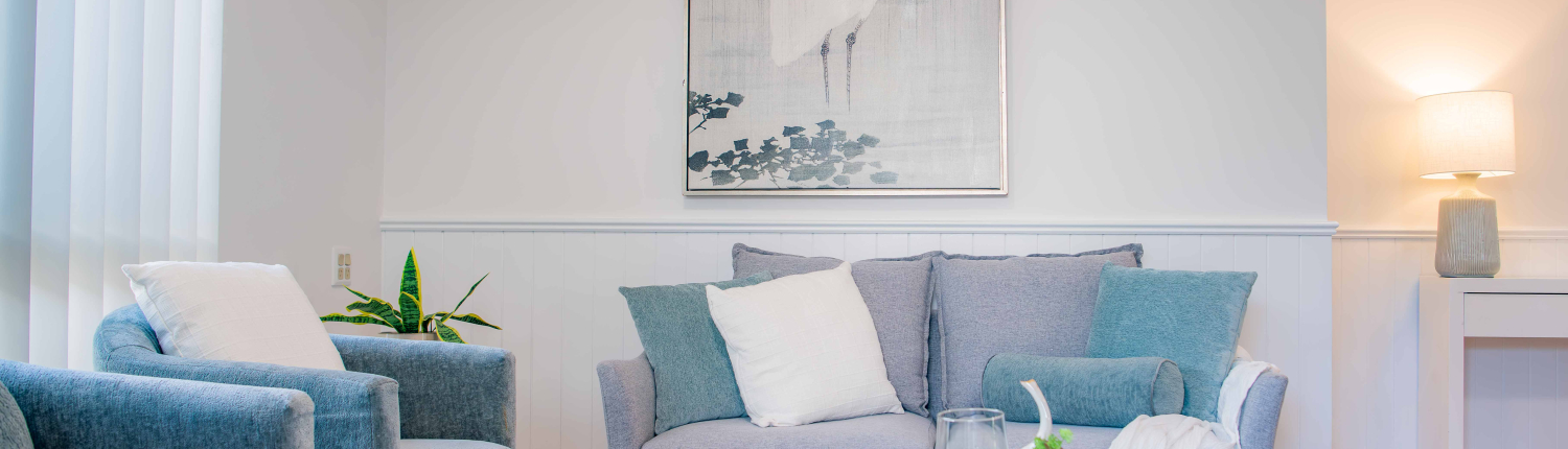 Lounge room with white walls, a bird print on the wall and petite grey 2-seater lounge