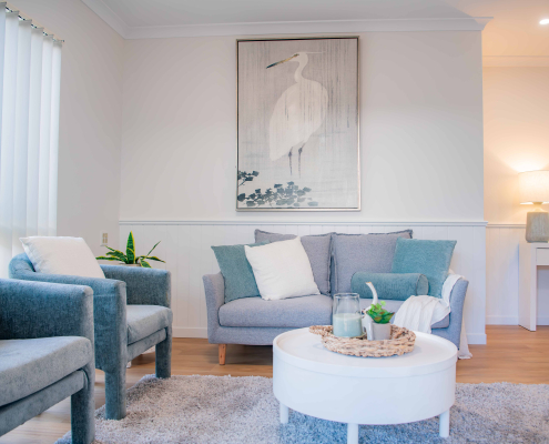 Lounge room with white walls, a bird print on the wall and petite grey 2-seater lounge