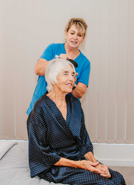Older lady in a dressin gown having her hair brushed by a carer