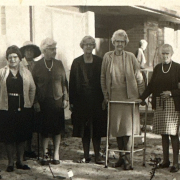 7 elderly women and one man posing for a photograph outside a building. The photograph is sepia and was taken in 1969