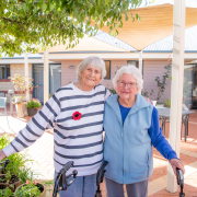 Two older ladies smiling for the camera standing in a courtyard with their arms around eachother's backs