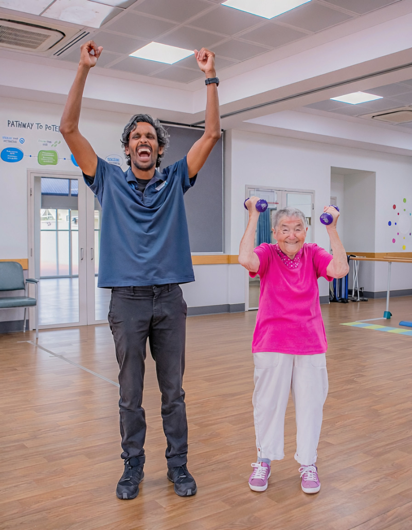 Capecare physio Marlon with Community client Kath A tall slim man standing next to a small older lady. Both have their hands in the air and are smiling and laughing. the lady is holding small hand weights and he is her physio
